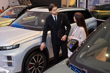 Adult Central Asian male auto dealer telling female customer about car wheel size describing...