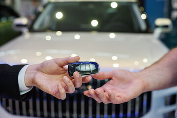 Close up on auto dealer hand giving smart key to male customer buying new vehicle at car dealership...