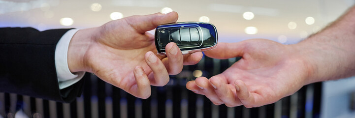Close up on auto dealer hand giving smart key to male customer buying new vehicle at car dealership center