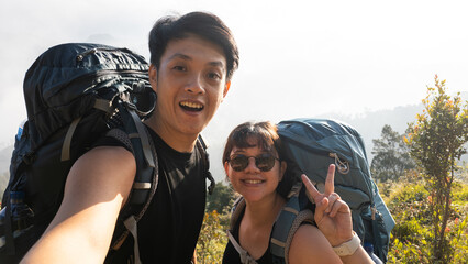 Happy Young asian couple wearing carrier backpack is doing hiking activity together at Mount Prau,...