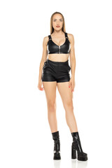 Fototapeta premium Beautiful blond woman in leather shorts, bra and boots on a white background. Front view.