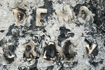 Burned wood letters spelling democracy sit in pile of ashes