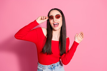 Portrait of pretty young girl touch sunglass dance red top isolated on pink color background