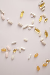 A scattering of tablets and capsules of dietary supplements with omega 3 on a plain background flat view from above