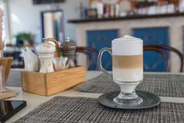 A cup of coffee sits on a table with a salt and pepper shaker and a napkin