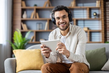 Hispanic man enjoying digital content on tablet while relaxing at home, wearing headphones and smiling
