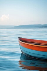 Naklejka premium Vibrant orange and blue boat floats serenely on calm water with distant mountains, a perfect scene of tranquility.