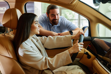 Side view of happy woman behind wheel of vehicle with beige leather interior testing demo car,...