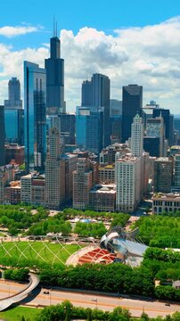A park with green trees and lawns in downtown Chicago. Tall skyscrapers and historic buildings. Aerial view. Vertical video.
