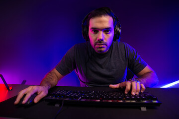 Smart gaming streamer concentrating gaming players trying to pass the level at mission completed, using headset and mic for communicate others on streaming live at neon lighting studio room. Surmise.