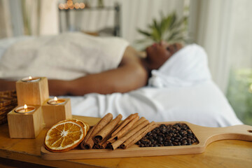 African American person relaxing in spa setting with candles, coffee beans, cinnamon sticks, and...