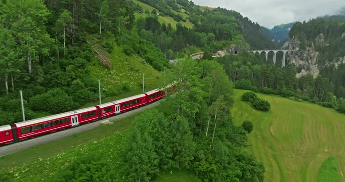 Aerial drone shot red train passing through famous mountain in Filisur, Switzerland. Drone footage of train traveling between mountains in Swiss countryside, Swiss mountain. Aerial drone Switzerland
