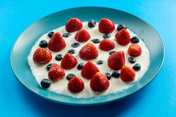 Strawberries and blueberries in a blue plate with cream on a blue background