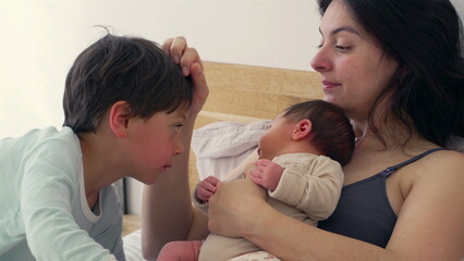 Mother holds her baby close while the older sibling leans in to look, highlighting the close-knit family bond. The scene reflects warmth, care, and the loving connection between mother and children