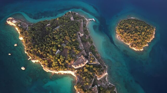 An aerial view of an island with lush vegetation and a fortress-like structure, surrounded by crystal-clear turquoise water