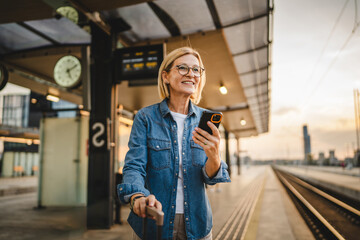 Mature woman wait for the train, use cellphone and walk with suitcase