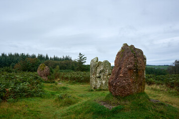 A peaceful scene with people by rocks and a stone sculpture in a serene landscape with trees and greenery, creating a balanced composition.