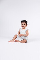 Portrait of a cute little baby girl seating on floor wearing white dress isolated on white background