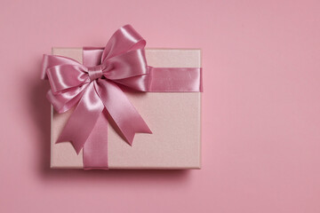 Gift box with bow on dusty pink background, top view