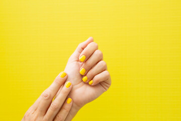 Woman's hands with yellow painted nails on a yellow background