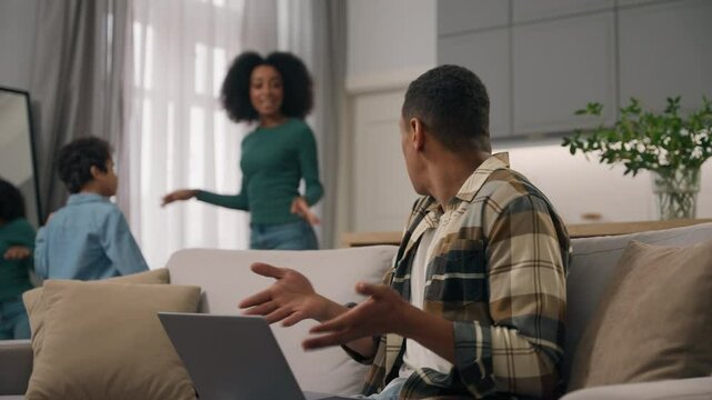 Angry desperate African American ethnic male dad man work online laptop device pc scold scream yelling on loud noisy woman mom female active dancing music little boy child kid son family home quarrel