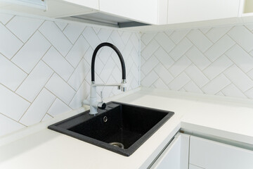 A black sink sits on a white counter in a modern kitchen