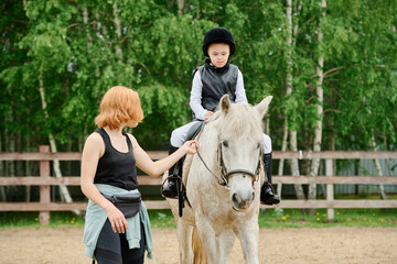 Trainer guiding child during horse riding lesson, with focus on child's posture and safety. Sunny...