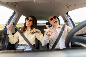 Perfect road trip. Excited spouses in sunglasses driving car, enjoying music and singing favorite...