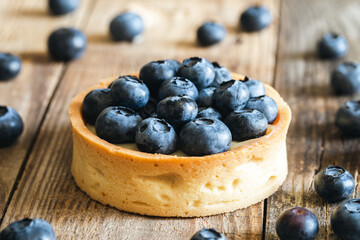 Homemade mini tart with blueberries and whipped cream on a wooden background, close up.