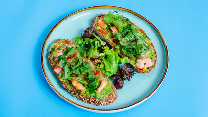 Two bruschettas with vegetables and shrimps in blue plate