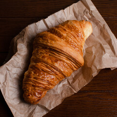 Crusty croissant on food paper on wooden table 