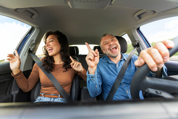 Car trip concept. Happy European couple husband and wife having fun while driving auto, listening...