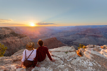 A man and a woman sit at the edge of the Grand Canyon at sunset minutes