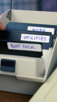 A user flips through his floppy disk caddy and locates the SPYWARE disk. Vintage computer user concept. Vertical orientation.  	