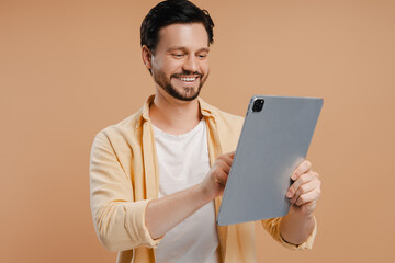 Cheerful bearded man using digital tablet on beige background © Maria Vitkovska