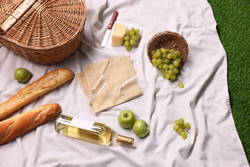 Picnic basket, different snacks and wine on green grass outdoors, above view