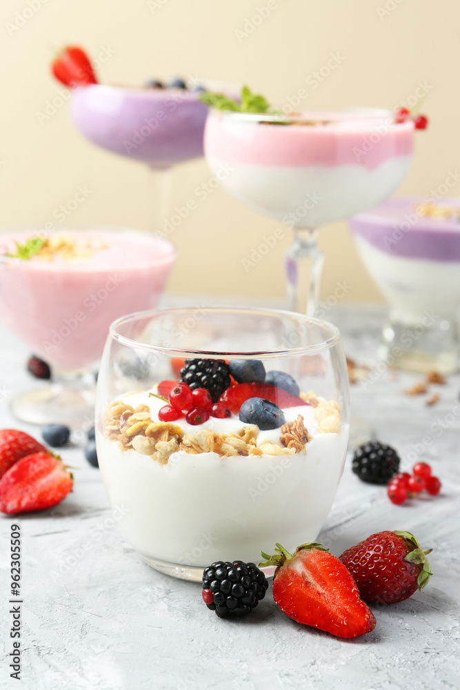 Poster Different tasty yogurts with fresh berries and granola in glass dishware on gray textured table, closeup