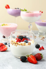 Different tasty yogurts with fresh berries and granola in glass dishware on gray textured table, closeup