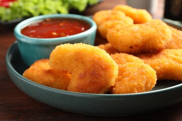 Plate with hot chili sauce and nuggets on wooden table, closeup