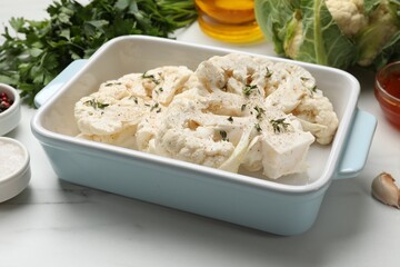 Uncooked cauliflower steaks and products on white marble table, closeup