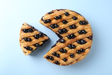 Cut homemade blueberry pie on light blue background, top view
