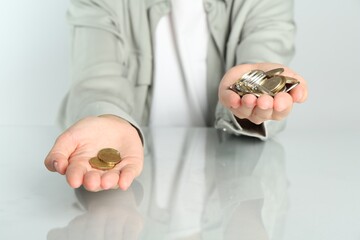 Financial inequality. Woman comparing coins in hands at white table, closeup