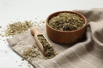 Dried oregano in bowl and scoop on white table