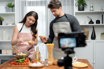 Couple chef influencers cooking special homemade of spaghetti with tongs taking to frying pan, putting seasoning and tasty sauce to make good flavor, recording on camera with live chanel. Postulate.