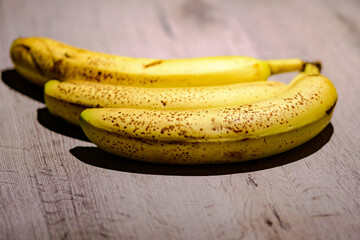 Photo of a set of 3 ripe bananas with brown spots on a gray table.