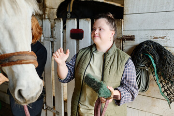 Woman assisting with grooming horse inside barn, showing attention and focus while using various...