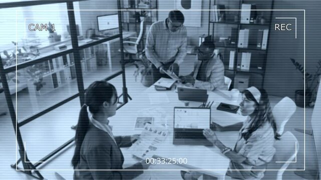 Surveillance camera shot of multiracial businesspeople gathering around table in office to discuss documents at meeting