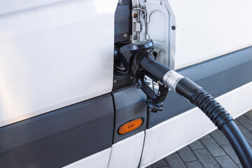 Closeup of a fuel nozzle in the car tank. Process of refilling a white transporter bus at a gas...
