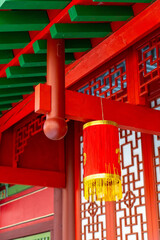 A bright red lantern adorned with golden fringe hangs from a beautifully designed structure featuring ornate architectural details