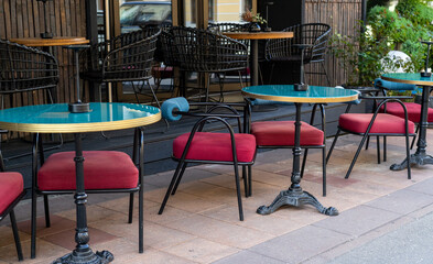 A row of stylish tables with vibrant surfaces and matching red chairs invites customers to enjoy the outdoors in a lively urban environment